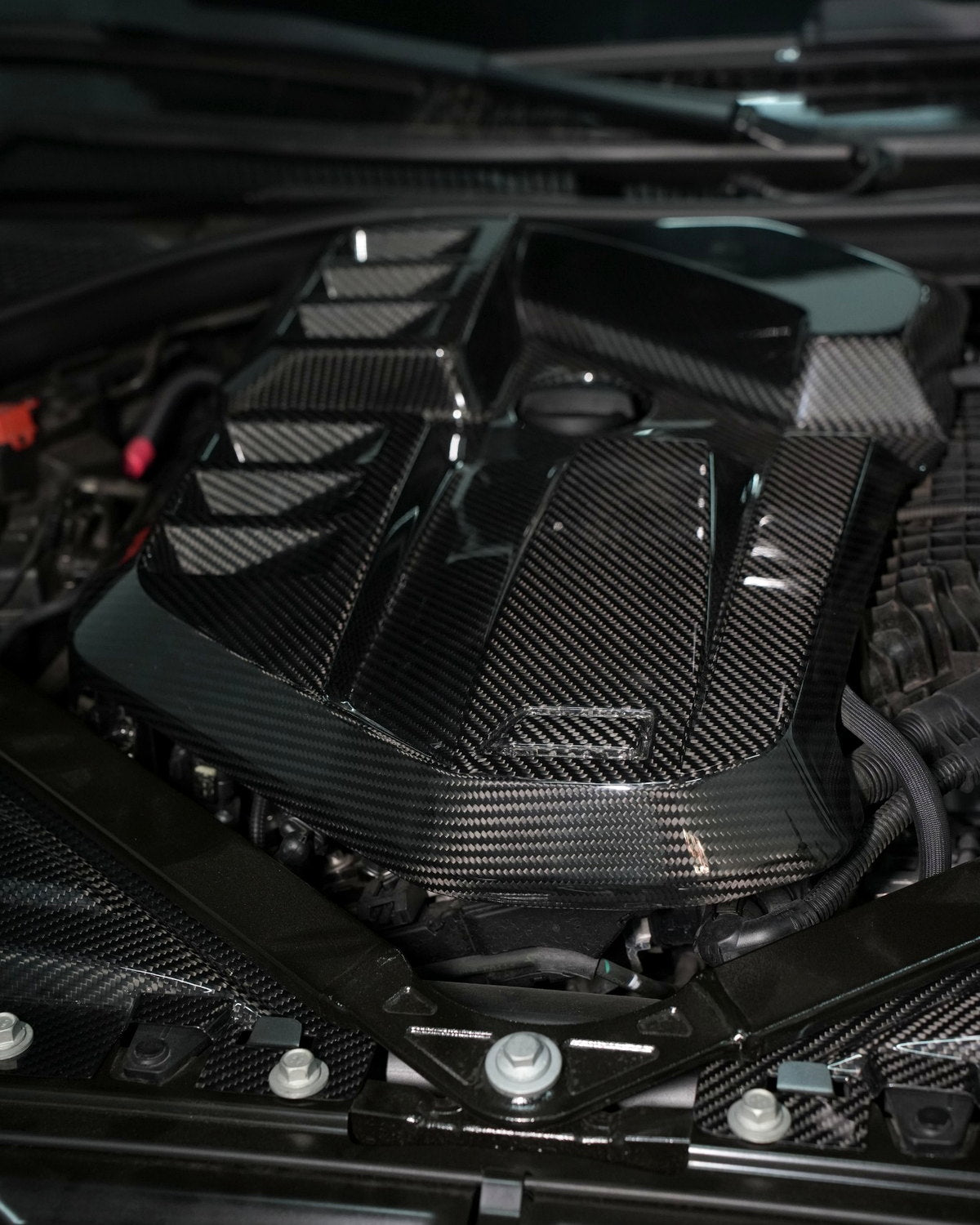 Gloss carbon fiber engine cover detail in a BMW G80 M3 engine bay