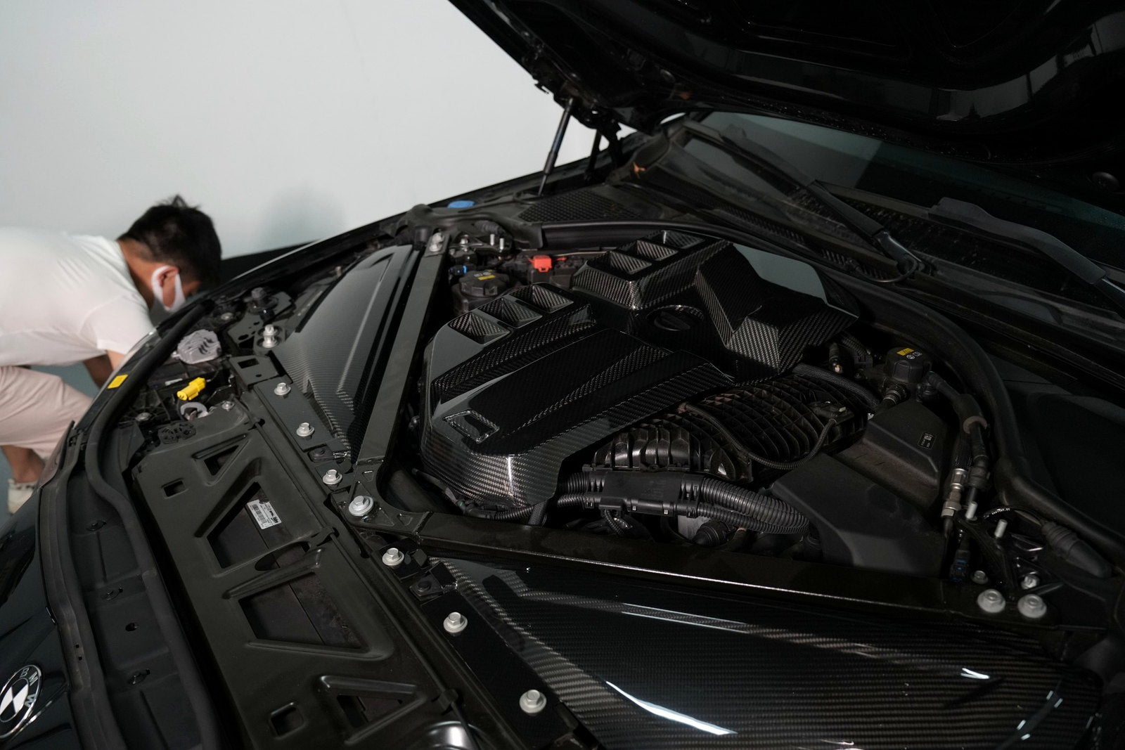 Technician test-fitting a carbon fiber engine cover on a BMW G80 M3